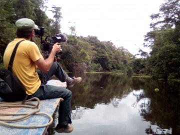 A filmmaker sitting on a pier films a lake and forest