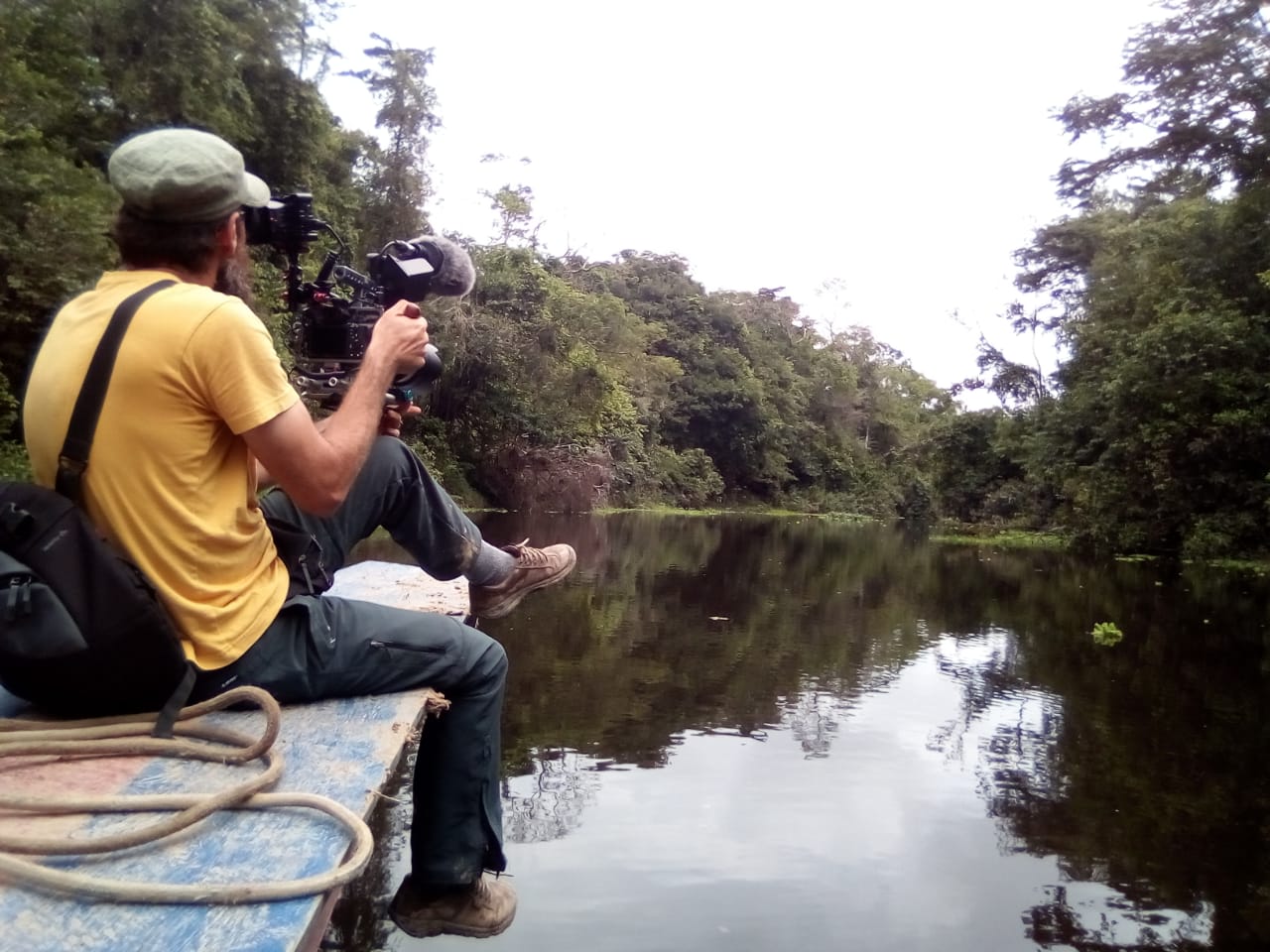 A filmmaker sitting on a pier films a lake and forest