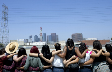 A group of women hold each other while looking at a city scape, emphasizing sisterhood