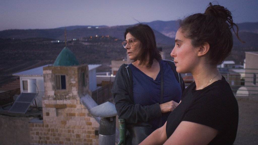 A still from the movie BYE BYE TIBERIAS, featuring filmmaker Lina Soualem and her mother returning to their native Palestinian village - the two overlook the village from a lookout post