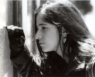A black and white photo of a woman looking through a window